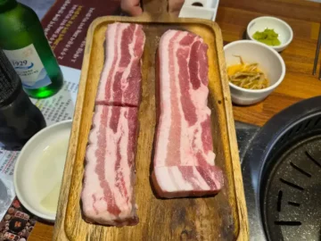 신선한 돼지고기 오겹살이 두툼하게 썰려 나무 도마 위에 놓여 있습니다.