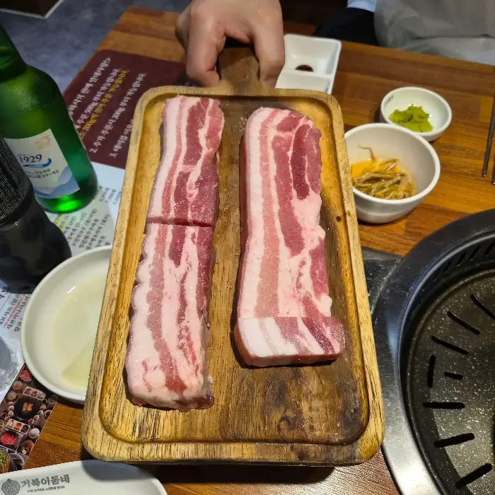 신선한 돼지고기 오겹살이 두툼하게 썰려 나무 도마 위에 놓여 있습니다.