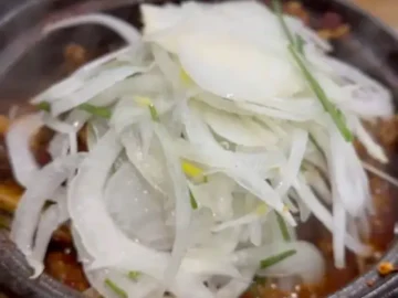 뜨겁게 끓고 있는 매콤달콤한 갈비찜 위로 얇게 썬 양파와 파가 듬뿍 올라가 있는 모습