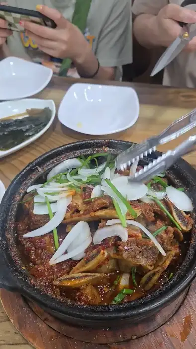 두 사람이 집게와 젓가락을 이용해 푸짐한 갈비찜을 덜어내고 있는 모습