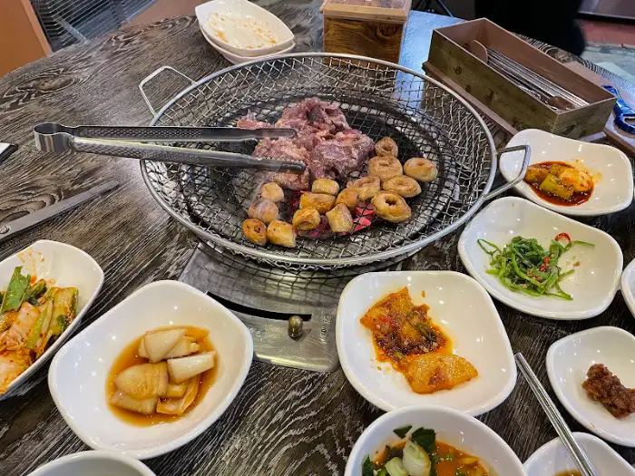 숯불 위에서 노릇하게 구워지고 있는 막창과 다양한 반찬들