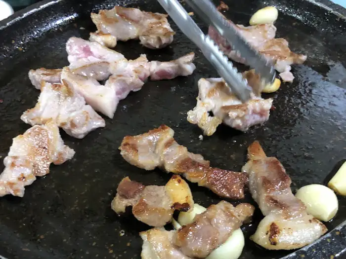 불판 위에서 노릇하게 구워지는 삼겹살과 마늘