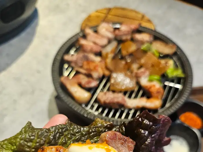 불판 위에서 맛있게 익어가는 고기와 쌈 채소