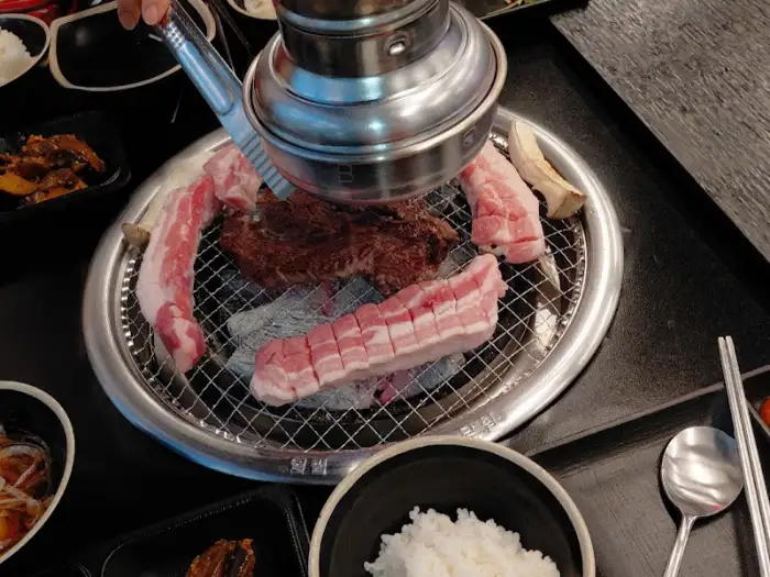 팔삼정육식당 오학점의 두툼한 생삼겹살이 숯불 위에서 구워지고 있는 모습