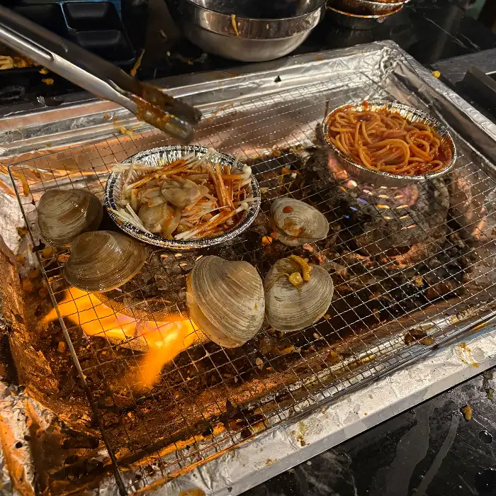 조개와 파스타, 삼겹살 등이 숯불 위에 올라가 있는 모습