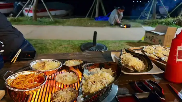야외 테이블에서 조개구이를 즐기는 모습과 뒤편의 바다 풍경
