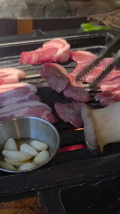 잘 달궈진 불판 위에서 지글지글 익어가는 고기들. 옆에는 통마늘과 큼직한 새송이버섯이 놓여있습니다.