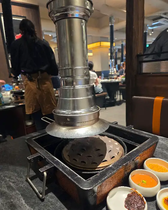 식당 내부의 모습. 연통이 달린 불판과 은은한 조명, 그리고 손님들이 식사하는 모습이 보입니다.