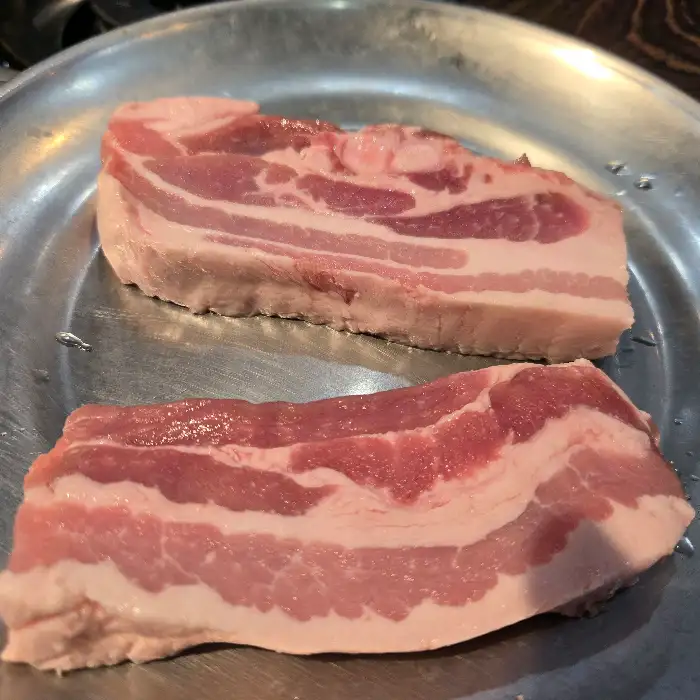 신선한 삼겹살 두 덩이가 접시에 놓여 있습니다. 두툼한 지방과 살코기 비율이 먹음직스럽습니다.