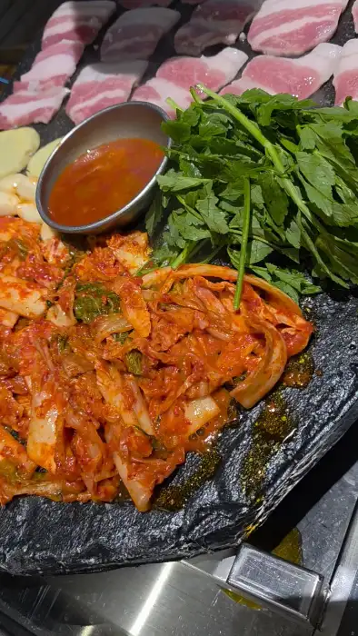 돌판에 구워지는 고기와 김치, 소스, 채소