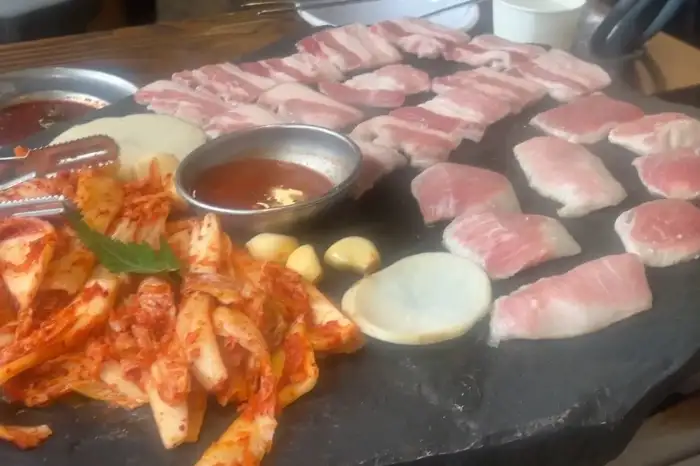 돌판 위에 구워지고 있는 삼겹살과 묵은지, 쌈무, 마늘, 쌈장