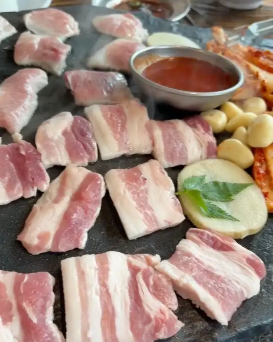 돌판에 가지런히 놓인 신선한 삼겹살과 묵은지, 마늘, 양파 조각