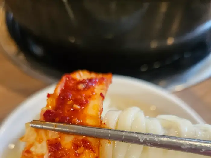 젓가락으로 집어든 매콤한 김치와 칼국수 면