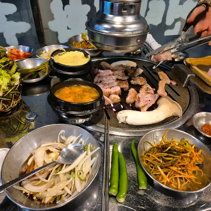 연탄불 위에서 익어가는 삼겹살과 항정살, 그리고 곁들임 찬들