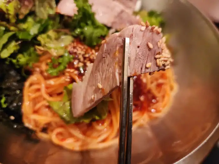 집게로 비빔국수의 고기를 들어 올리는 모습