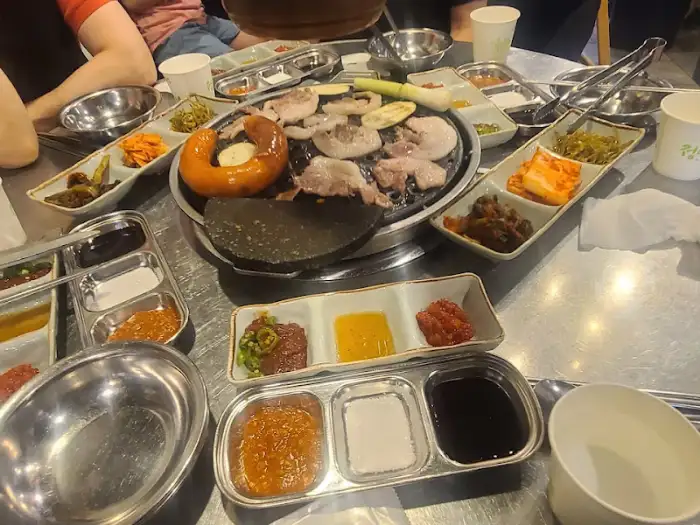 불판 위에서 구워지고 있는 고기와 다양한 곁들임 반찬, 소스 접시들이 차려진 식탁 모습