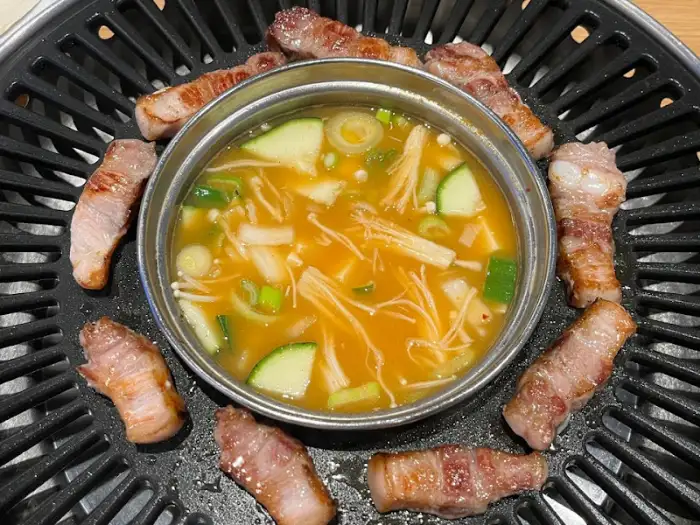 숯불 그릴 중앙에 놓인 사골 라면 찌개와 주변에 둘러싸인 구워지는 고기