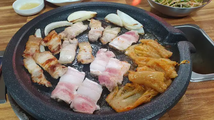 가스 철판 위 노릇하게 구워지고 있는 삼겹살과 묵은 김치의 모습