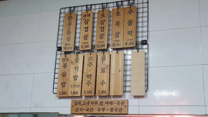 나무 패널로 만들어진 현대식육식당의 메뉴판, 다양한 돼지고기 및 식사 메뉴 가격 표시