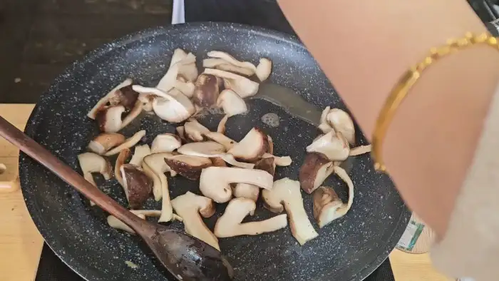 손이 참기름을 두른 팬에 버섯을 볶는 모습