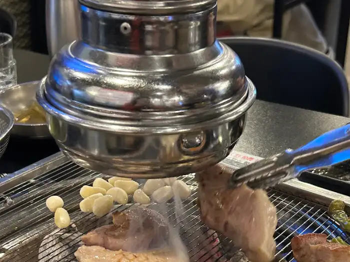 식껍 용산점 테이블 위 숯불구이 석쇠와 집게로 고기를 올리는 모습