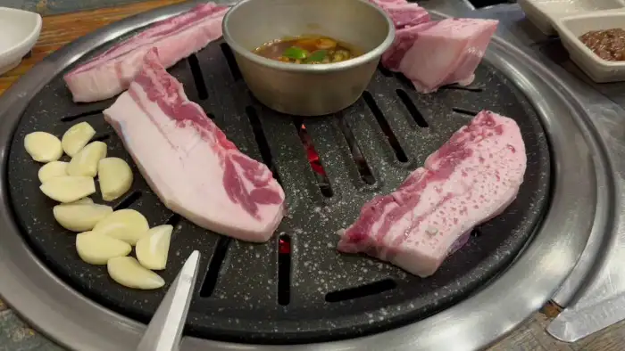 돼지고기 목살과 통마늘, 소스가 곁들여진 숯불구이 불판