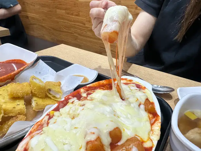 치즈가 듬뿍 올라간 쪼매매운떡볶이의 치즈오븐 떡볶이에서 치즈를 늘어뜨리는 모습