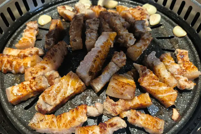 불판 위에서 익어가고 있는 두툼한 오겹살과 마늘