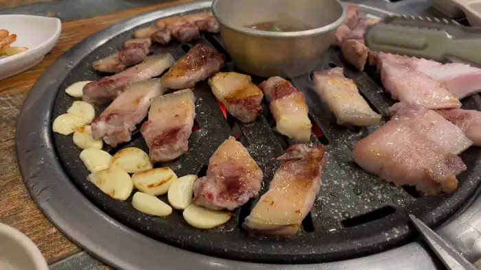 숯불 위에서 익어가는 두툼한 삼겹살과 통마늘, 곁들임 소스
