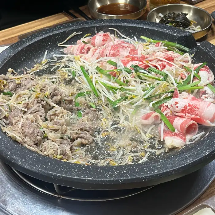 얇게 썬 돼지고기와 숙주나물이 함께 올려져 익고 있는 불판