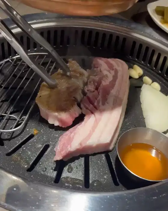 집게로 집어 돌판 위에서 굽고 있는 삼겹살 조각